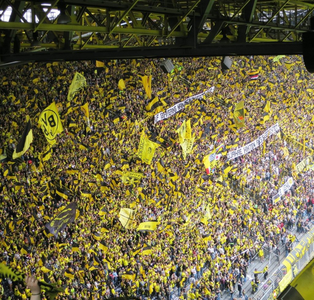 Dieses Bild zeigt volleTribünenränge im Signal Iduna Park und Fans, welche mit ihren schwarzgelben Fahnen dem BVB zujubeln.