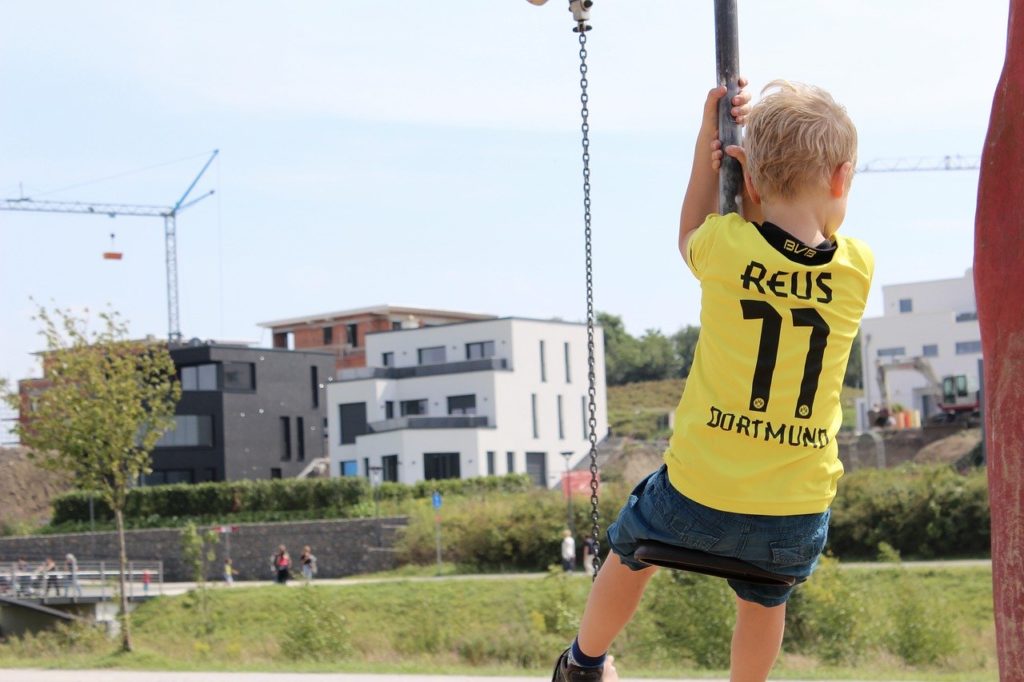 Dieses Bild zeigt einen jungen BVB Fan mit seinem Marco Reus T-Shirt, welcher auf einem Spielplatz auf einer Schaukel sitzt.